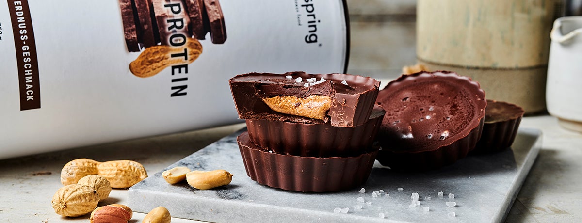 A photo of a stack of homemade Protein Peanut Butter Cups with the top cup broken open to reveal the peanut butter inside.