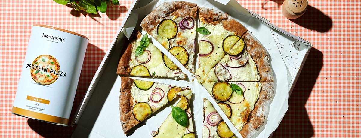 A pizza bianca rests on a sheet of white paper. The pizza is topped with thinly sliced zucchini