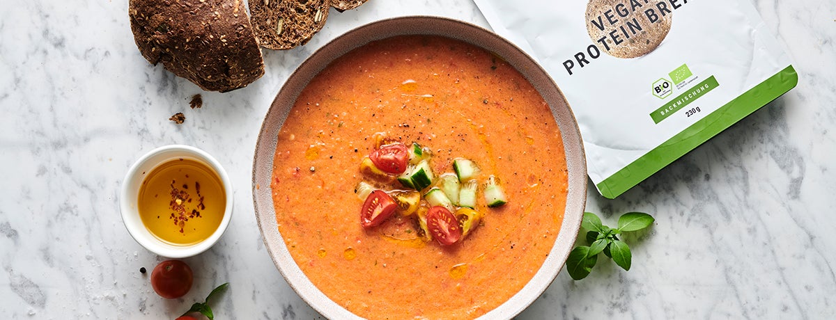 An enticing bowl of cooling gazpacho in a blended, flame-red color with diced cherry tomatoes and cucumbers as a garnish on top