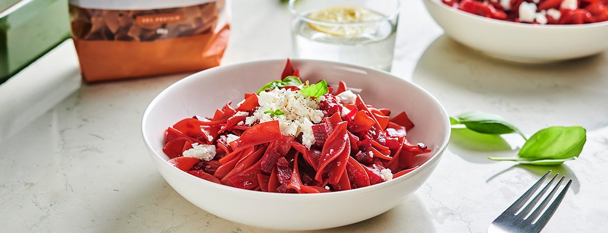 A bowl of bright red protein pasta with beet giving it the red color. It is topped with crumbled feta cheese.