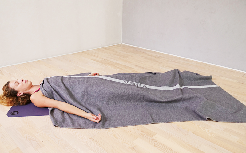 Donna esegue posizione del cadavere (Shavasana) con una coperta sopra