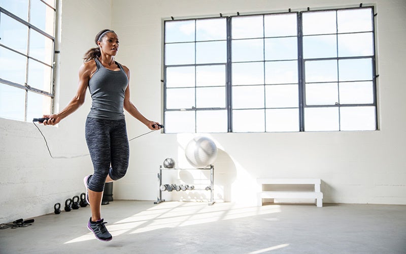 A woman of color in a white-walled gym setting using a jump rope to warm up