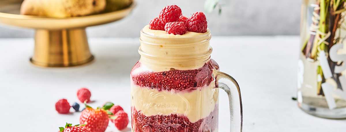 A layered vanilla raspberry shake with white and red layers, topped with fresh raspberries