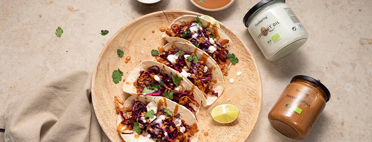 A photo of four jackfruit tacos with a peanut butter sauce drizzle on a tan plate