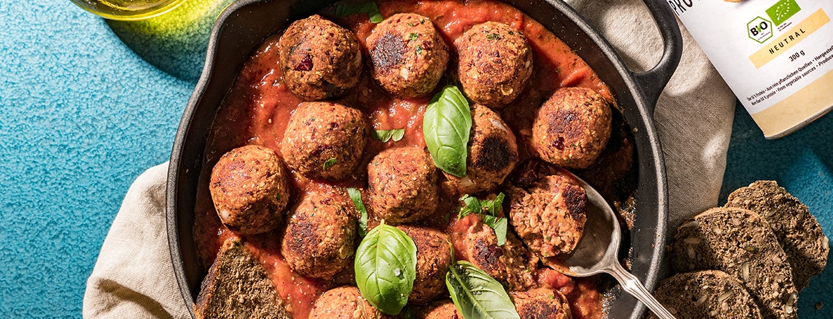 A cast-iron pan of vegan meatballs in a base of tomato sauce, garnished with a few whole basil leaves