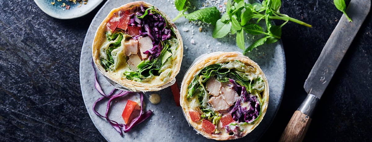 A photo of a wrap filled with chicken and vegetables, one of foodspring's recipes. Check out our recipes section for delicious ways to build healthy habits.