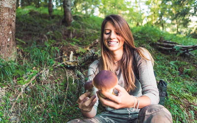 A smiling woman collects mushrooms during a nature walk