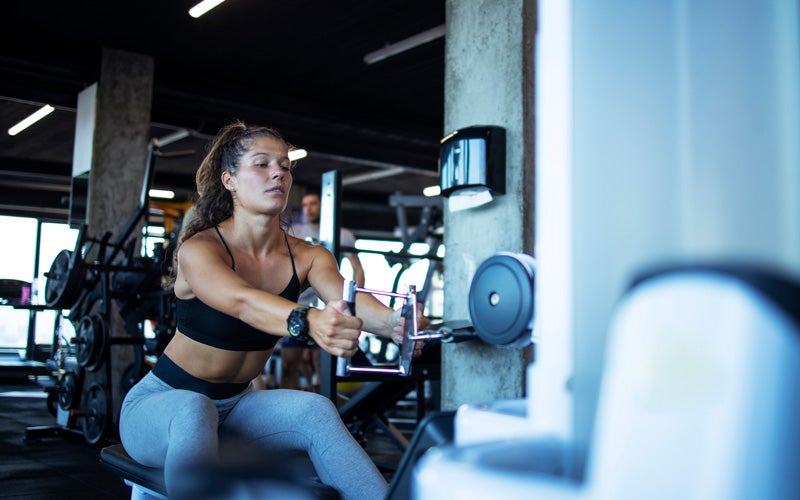 An athletic white woman in a sports bra and leggings works out on a rowing weights machine