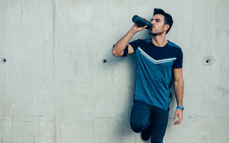 Läufer trinkt an einer Wand gelehnt aus seiner Wasserflasche