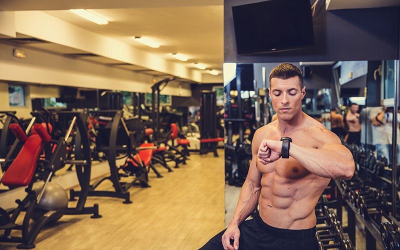 sportlicher Mann macht eine Trainingspause im Fitnessstudio und schaut auf seine Uhr
