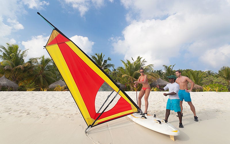 Surflehrer zeigt zwei Personen am Strand das Windsurfen