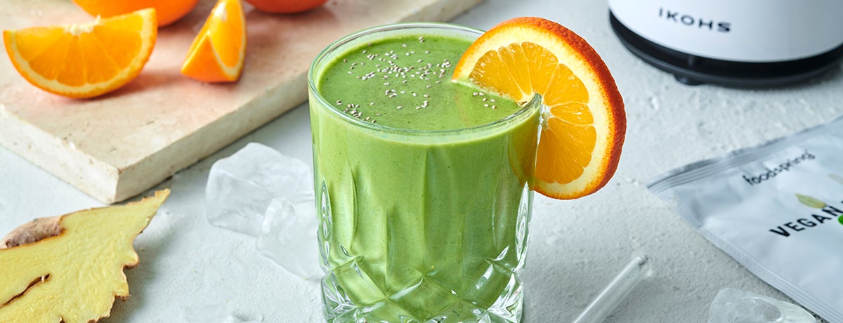 A photo of a glass of bright-green Hangover Green Smoothie with an orange slice hanging over the rim of the glass