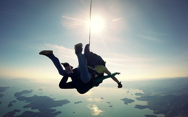Two people go tandem skydiving over a view of islands and sea.