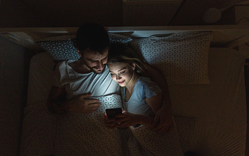 Pärchen liegt im Bett und schaut auf ein Smartphone