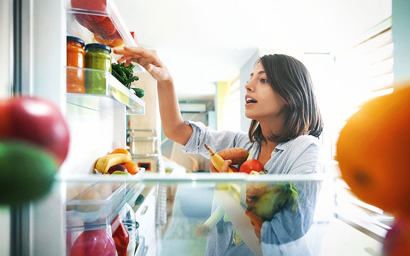 Eine Frau nimmt Gemüse aus ihrem Kühlschrank heraus
