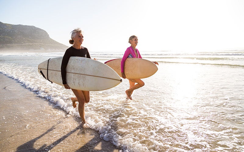 Zwei ältere Frauen mit Surfbrettern am Strand