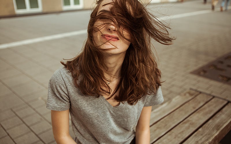 Eine Frau sitzt draußen und ihre Haare wehen im Wind
