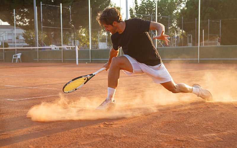 Un uomo gioca a tennis su terra rossa
