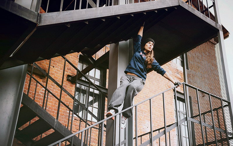 A white woman hangs on a stairwell and stands on a railing while doing parkour