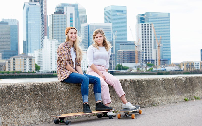 Zwei junge Frauen sitzen neben ihren Longboards