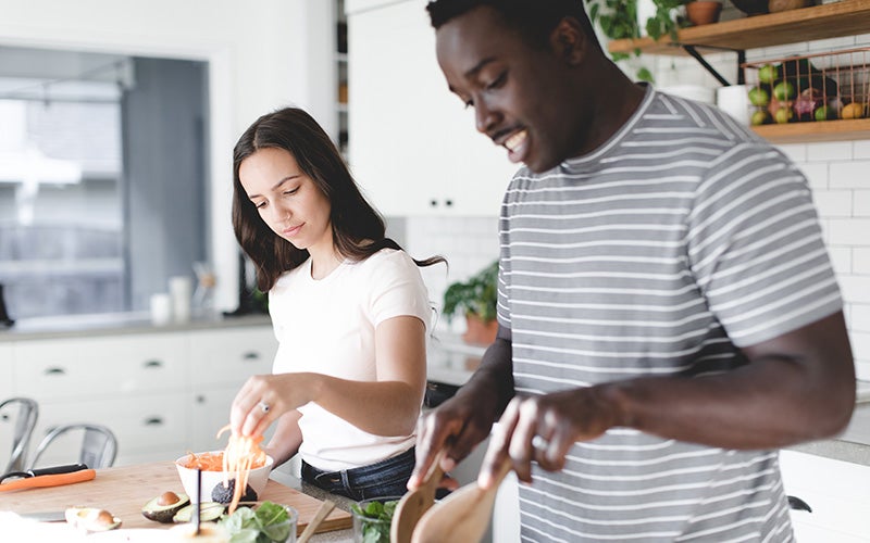 A Black man and a white woman cook together in a white kitchen
