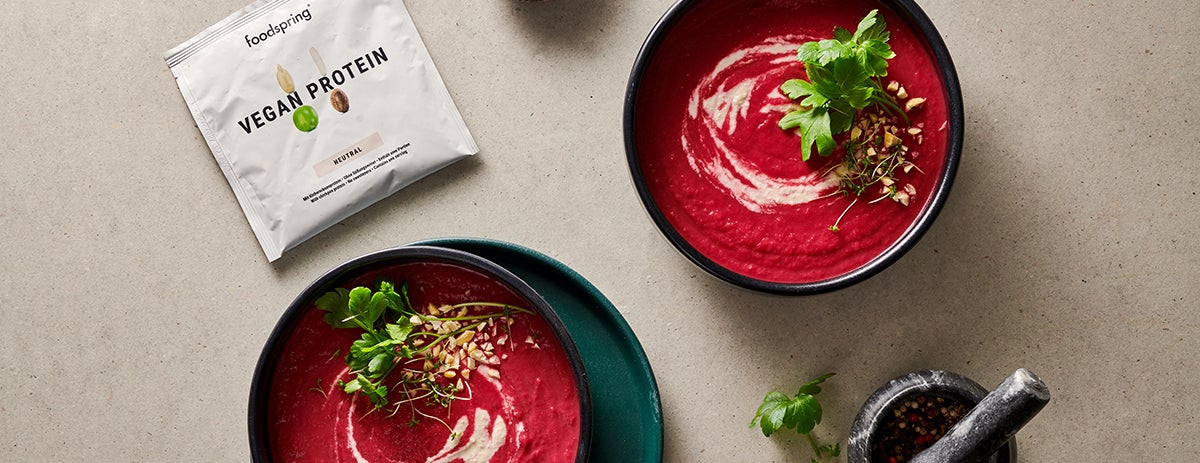 A bowl of vibrant red beet soup with a subtle white cashew swirl, topped with fresh herbs, making the most of fall vegetables.