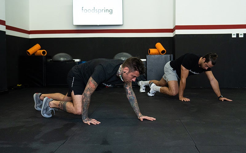 Two white men in foodspring t-shirts do zombie crawls for the foodspring Halloween workout