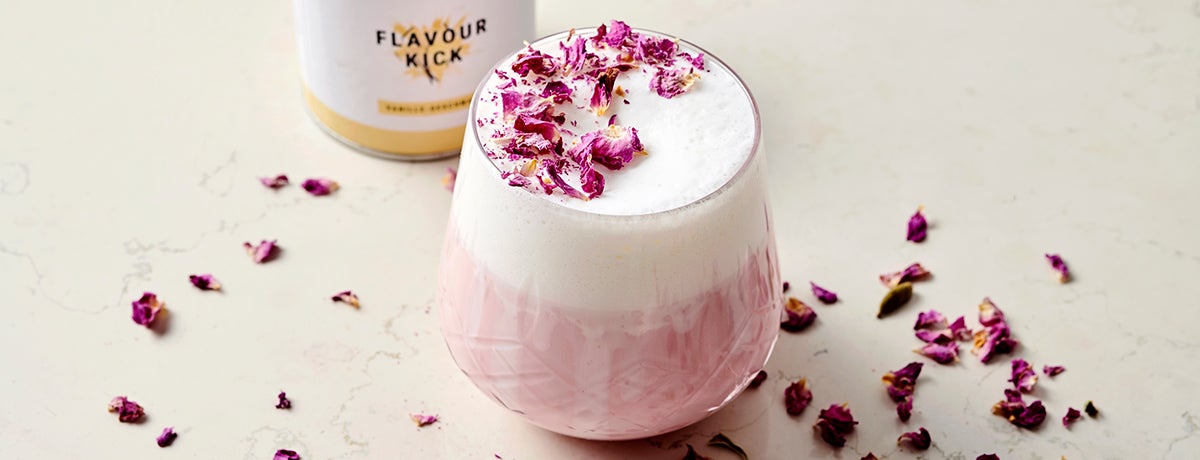 A glass of pink cardamom rose latte topped with dried rose petals