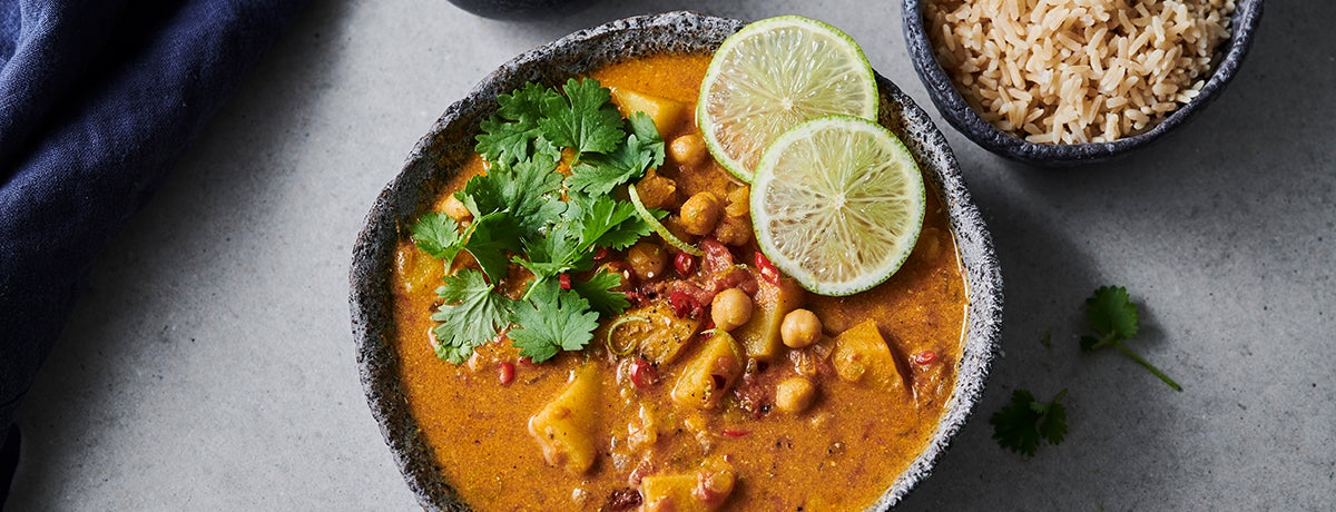 A stone bowl of vegan peanut stew with potatoes and chickpeas, topped with cilantro and paper-thin lime slices