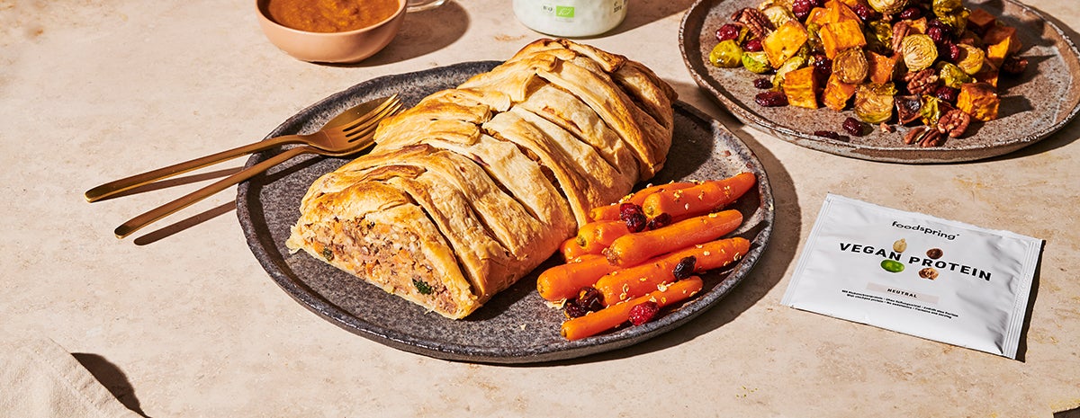 A plate holds a vegan beef Wellington with bright orange glazed carrots