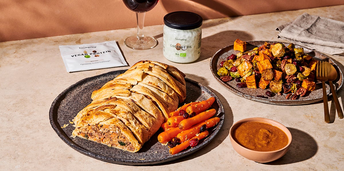 A plate of Vegan Beef Wellington sits on a stone countertop with bright orange carrots next to it.