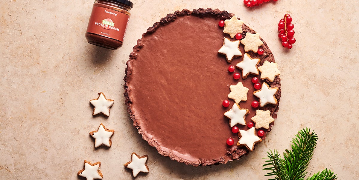 A Vegan Amaretto Chocolate Tart seen from above, decorated with a mix of star-shaped sugar cookies and bright red redcurrants.