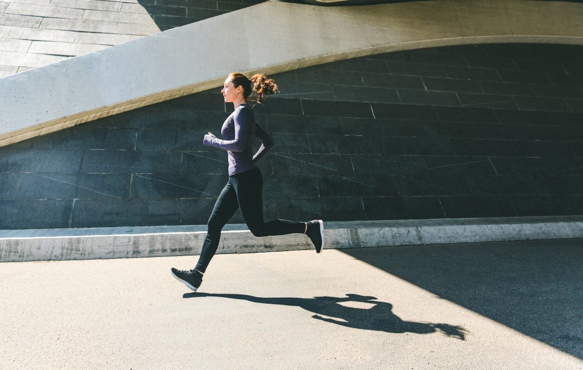 Woman jogging or running, side view with her shadow on the ground. Girl wearing sportswear doing fitness activities outdoors. Healthy lifestyle and sport concepts