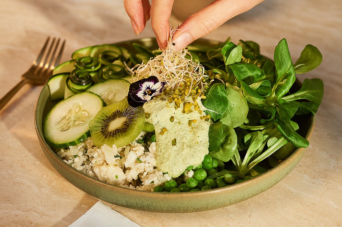 A white person's hand tops a green goddess bowl with sprouts. With dishes like these, staying vegan has never been easier!