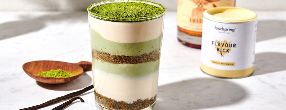 A glass full of layers of vegan matcha tiramisu, alternating between chocolatey brown, white yogurt, and green matcha-yogurt.