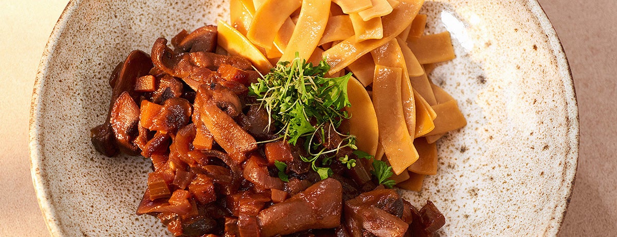 A plate of mushroom bourguignon accompanied by Protein Pasta and a topping of microgreens