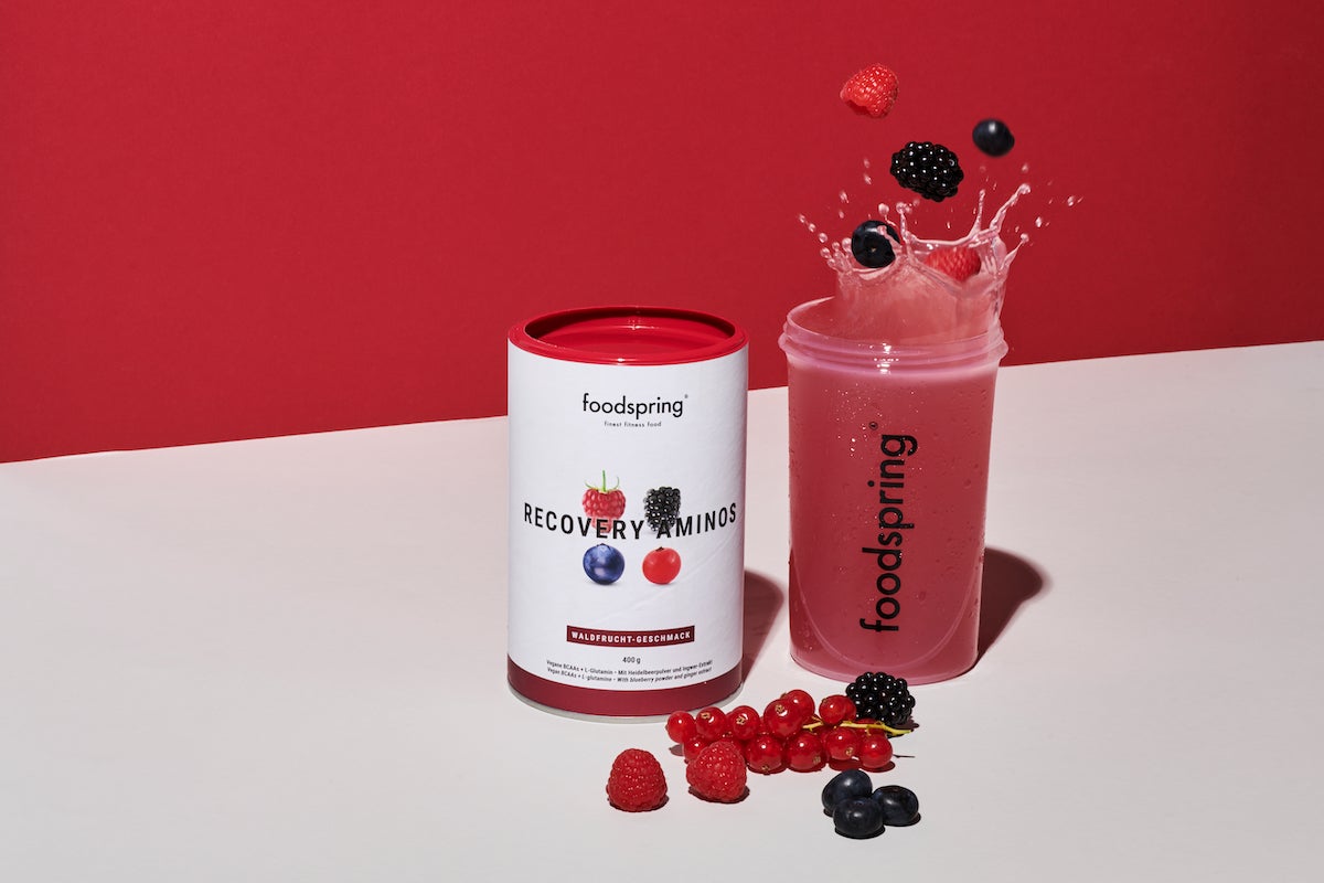 Recovery Aminos on colourful backdrop with shaker full of liquid and berries falling in.