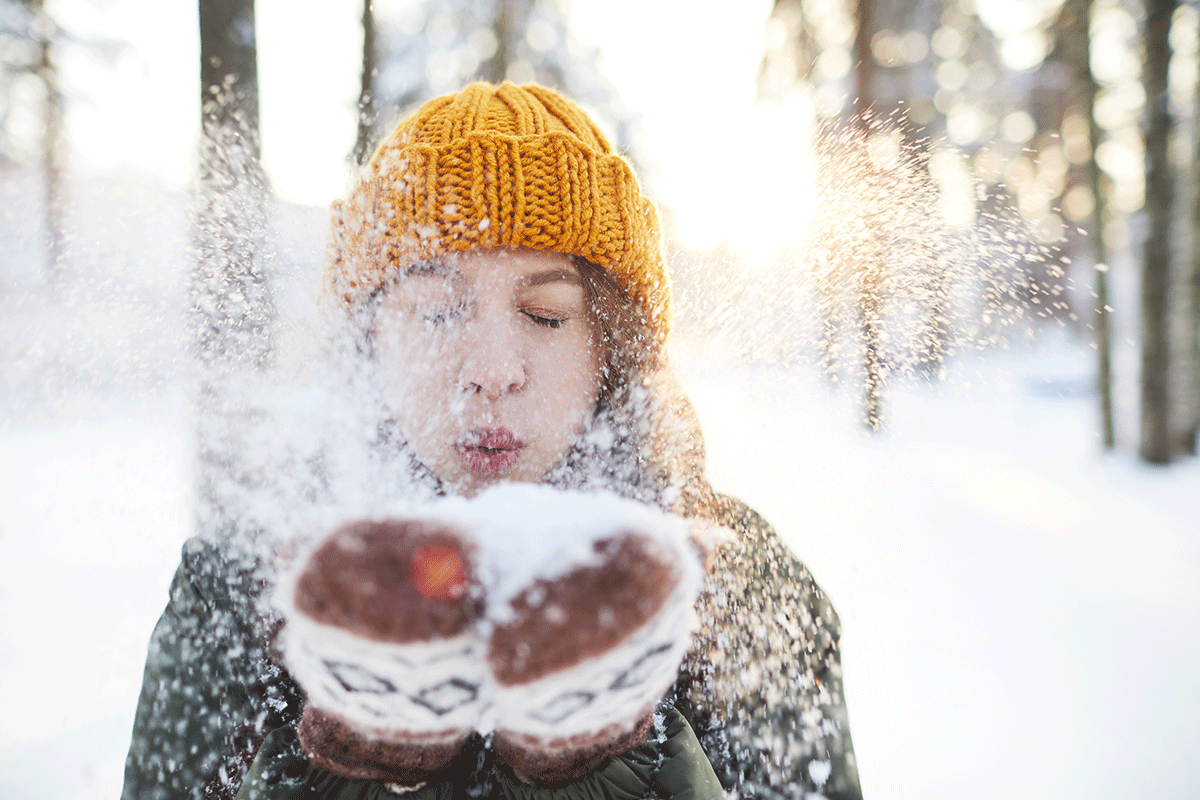 Una ragazza in un bosco d'inverno soffia sulla neve che tiene sulle mani