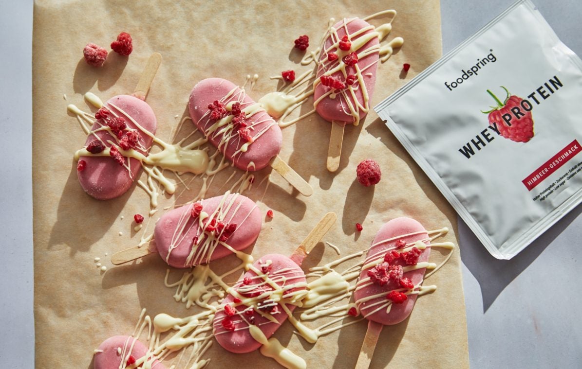 raspberry yogurt popsicles drizzled with white chocolate on a piece of parchment