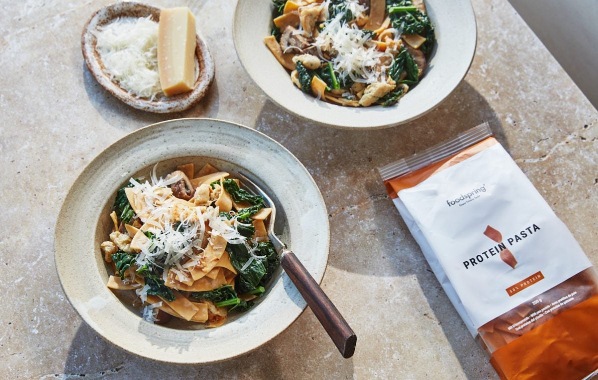 two bowls of sausage pasta with kale and mushroom and a plate of grated parmesan