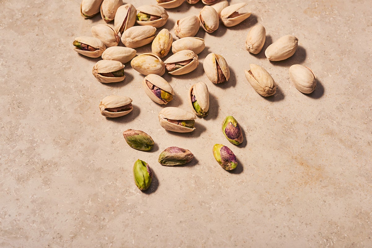 A scattering of pistachios, shelled and unshelled, on a beige table background.