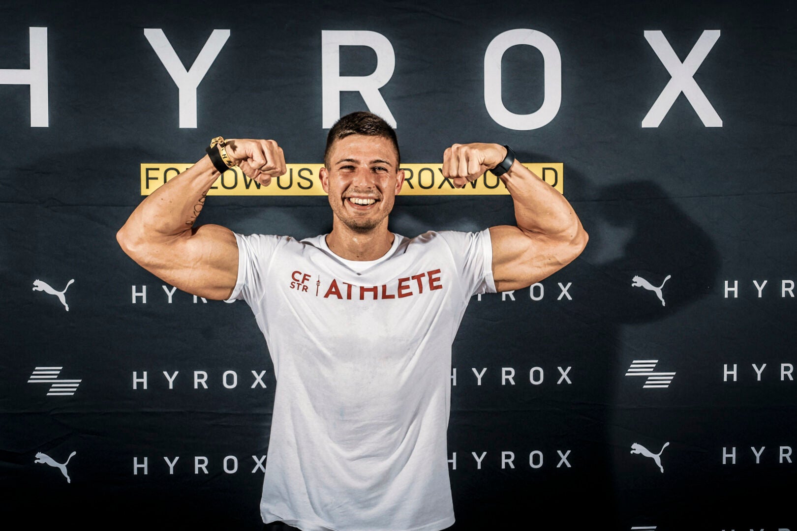 Hyrox athlete Julius Ise flexing in front of a Hyrox themed wall. 