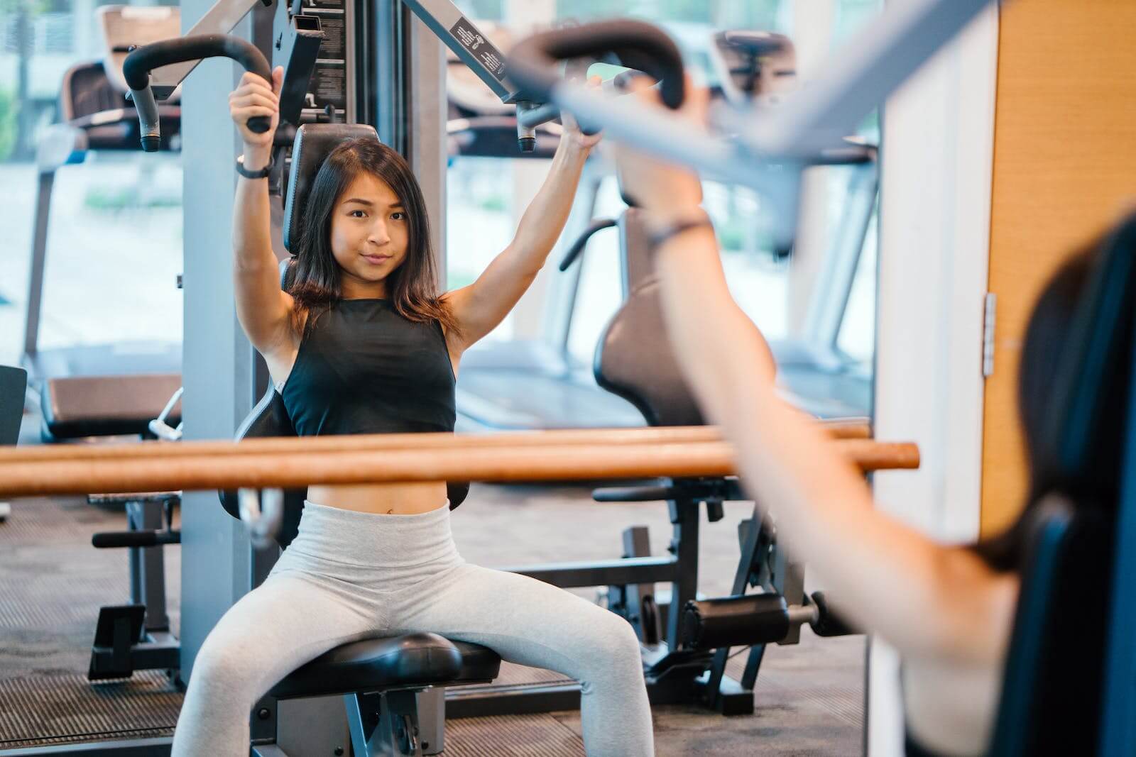 Eine Frau sitzt im Fitnessstudio, macht Armübungen und betrachtet sich im Spiegel