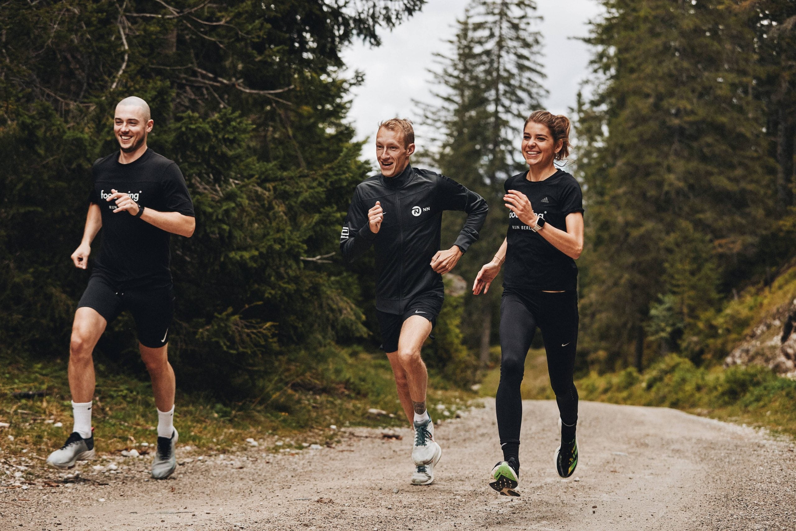 three runners on a wooded trail wearing black athletic clothing. Björn Koreman is in the center.