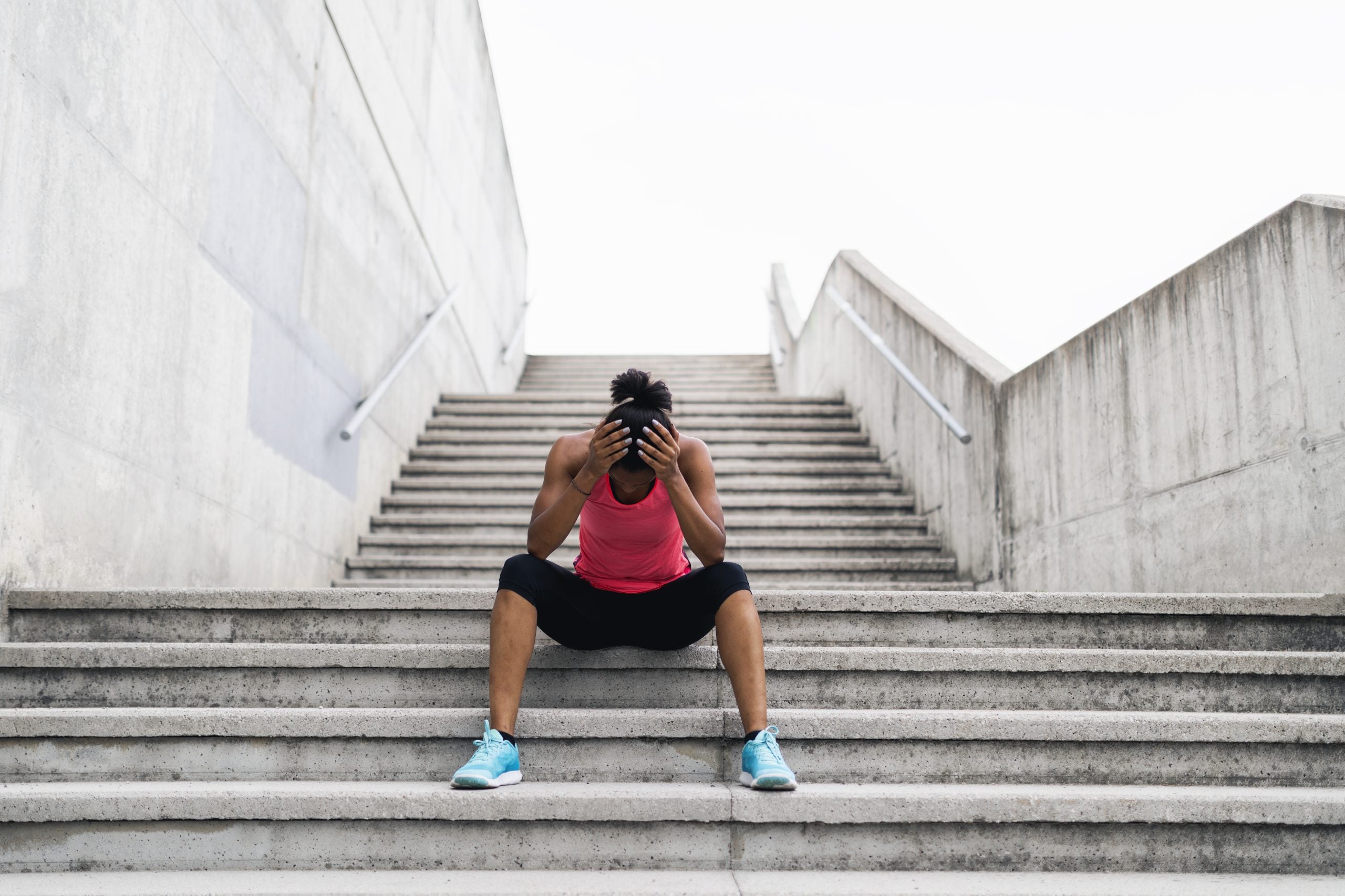 Woman helds her head sitting on a stair outside